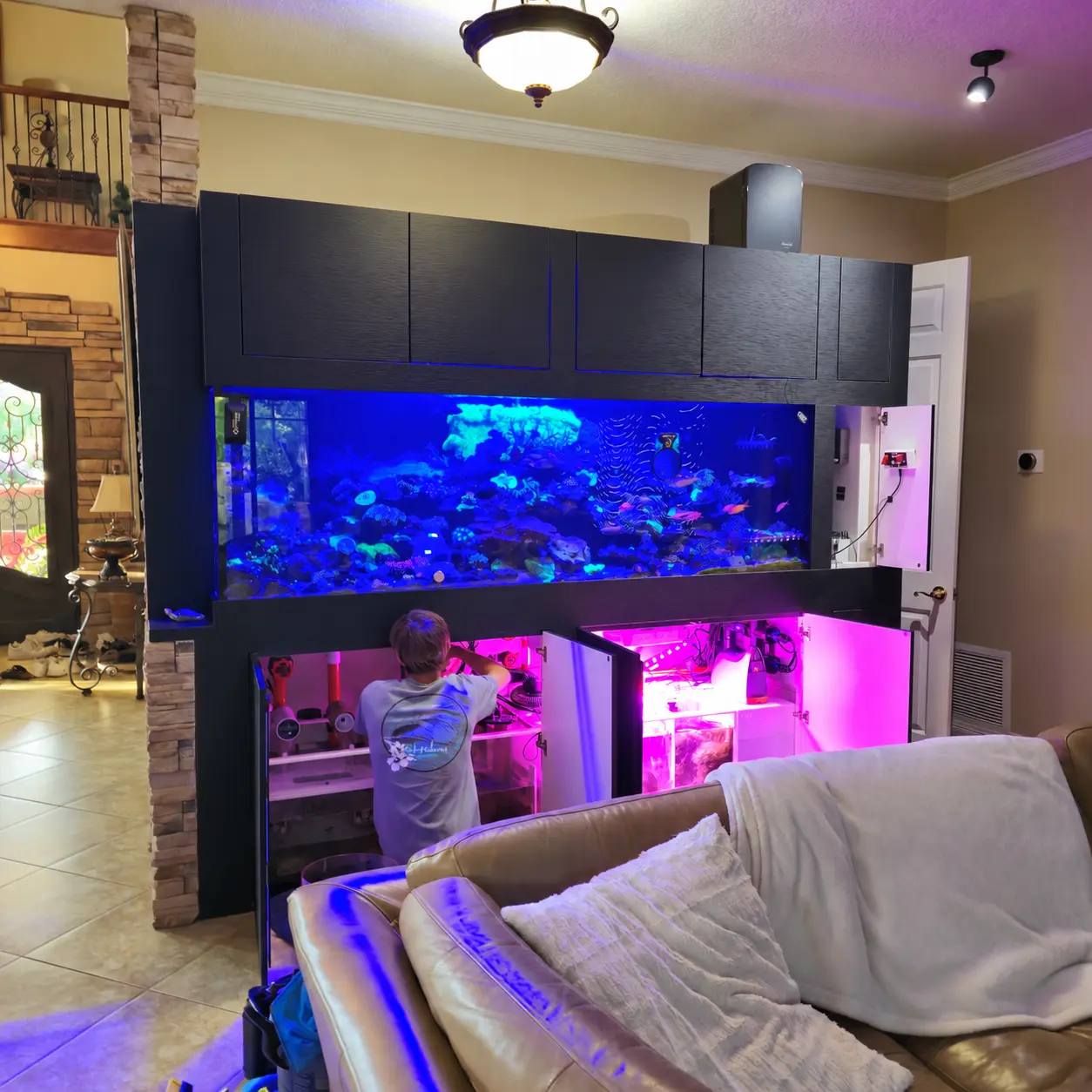 Technician working beneath a residential reef aquarium during installation and cleaning